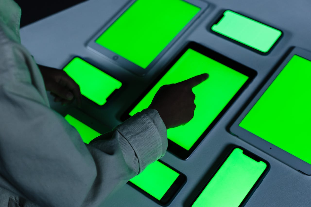 gallery-1 Person interacting with multiple green-screen electronic devices indoors.